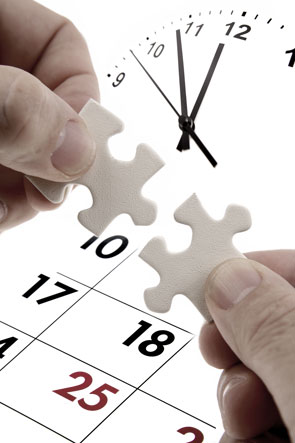 Mani che tengono due pezzi di puzzle combacianti, davanti ad un orologio e ad un calendario.
